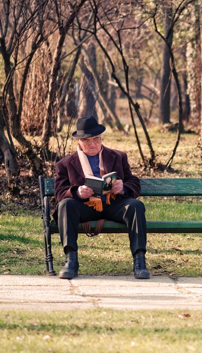 Ein Senior sitzt auf einer Parkbank und ließt ein Buch